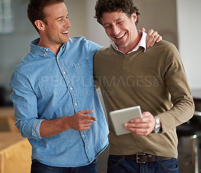 Buy stock photo Two male colleagues laughing at something on a digital tablet together