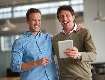 Buy stock photo Two male coworkers sharing something humorous on a digital tablet