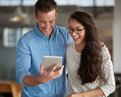 Buy stock photo Friendly colleagues laughing at something funny on a digital tablet at the office