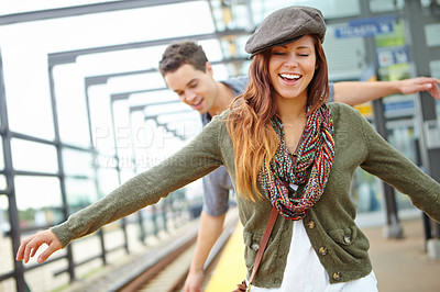Buy stock photo A smiling couple balancing along the railway of a train station with copyspace