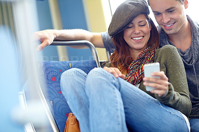 Buy stock photo Shot of a happy couple on the train looking at something on a cellphone