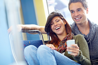 Buy stock photo Portrait of a laughing couple on a train with the girlfriend holding a cellphone and copyspace
