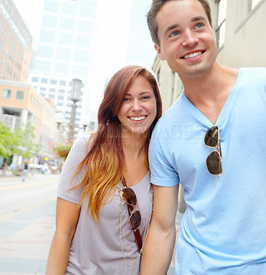 Buy stock photo A happy couple holding hands and walking along a city street with copyspace