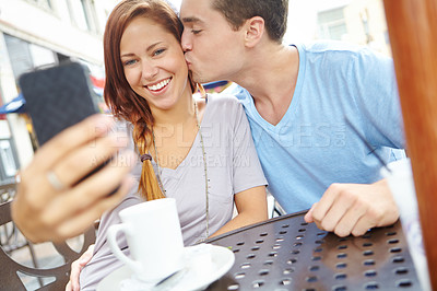Buy stock photo A happy couple sitting at a cafe taking a picture of themselves with a cellphone