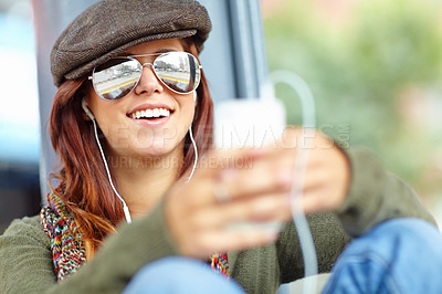 Buy stock photo Shot of a beautiful woman wearing sunglasses waiting at a train station and listening to music on her cellphone