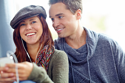 Buy stock photo Shot of a pretty girl listening to music on her phone while her boyfriend looks at her lovingly