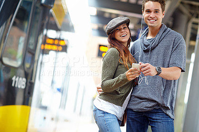 Buy stock photo Portrait of  happy couple listening to music on a phone while waiting fro a train with copyspace