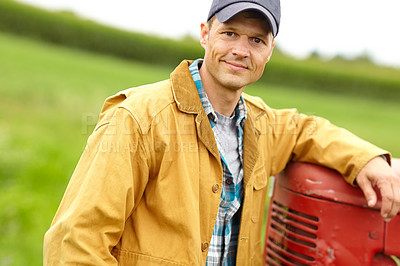 Buy stock photo Portrait of a smiling farmer with his arm resting on the hood of his tractor while he stands in an open field