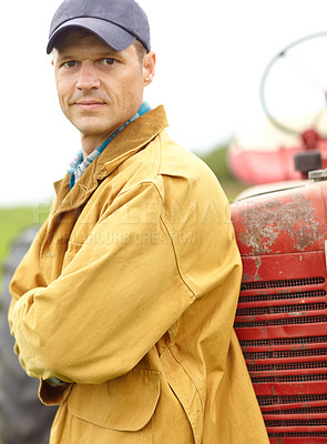 Buy stock photo Portrait of a farmer with his arms crossed while leaning against the hood of his tractor