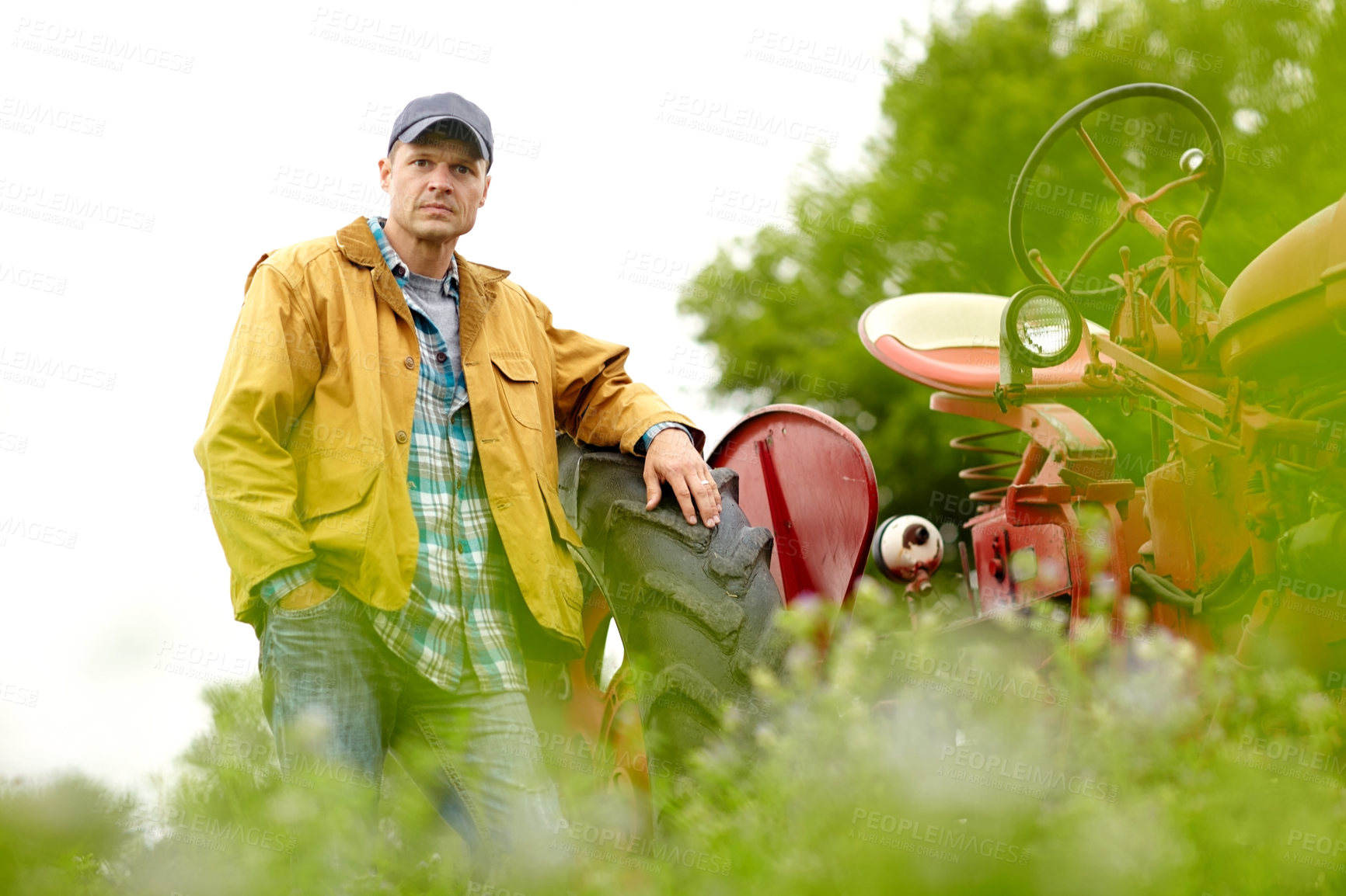 Buy stock photo Portrait of handsome farmer leaning on the tyre of his tractor in a field