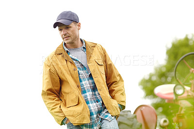 Buy stock photo Shot of a contemplative farmer walking in a field with his tractor behind him