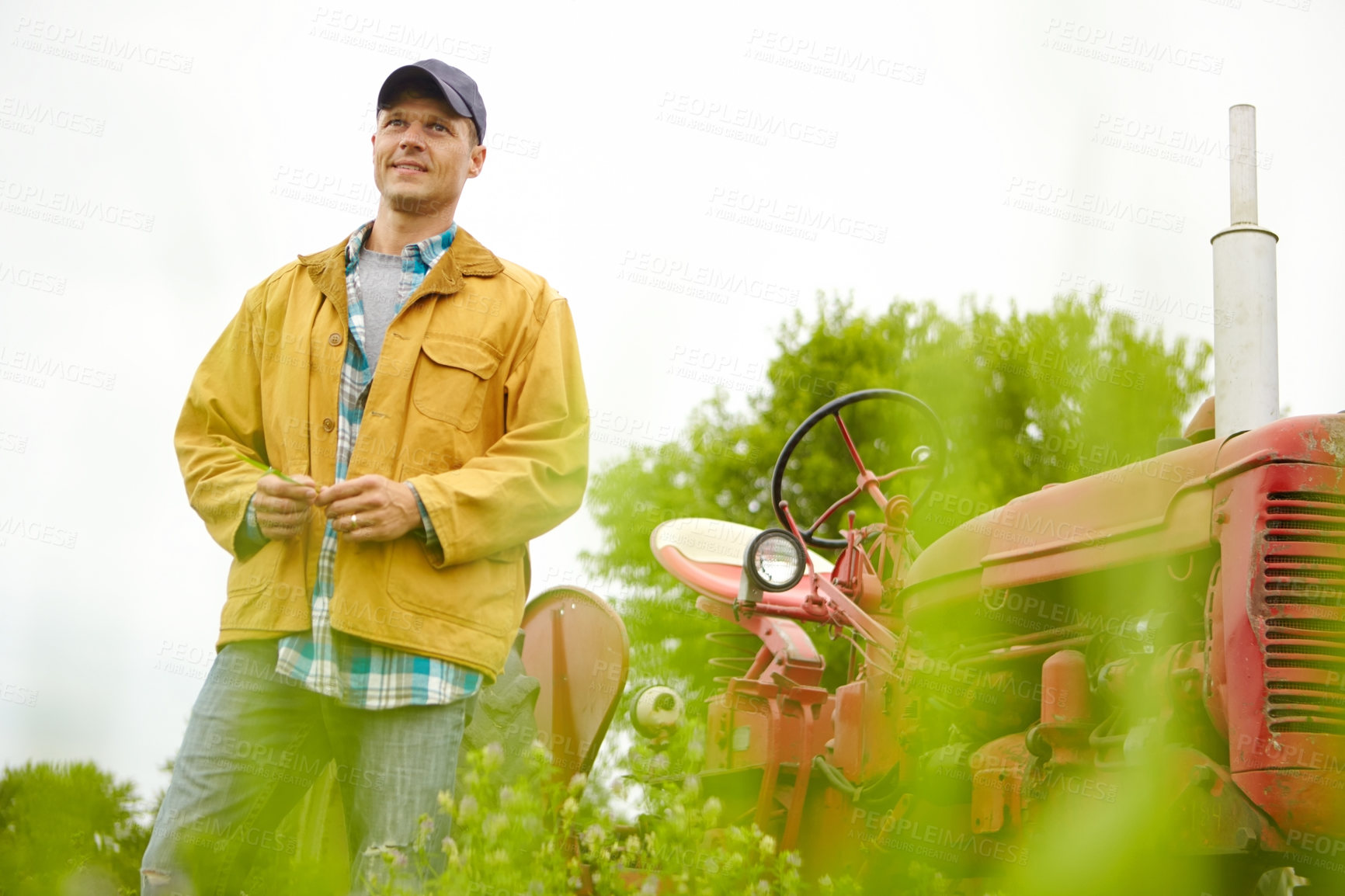 Buy stock photo Shot of a farmer standing in a field with his tractor beside him - Copyspace