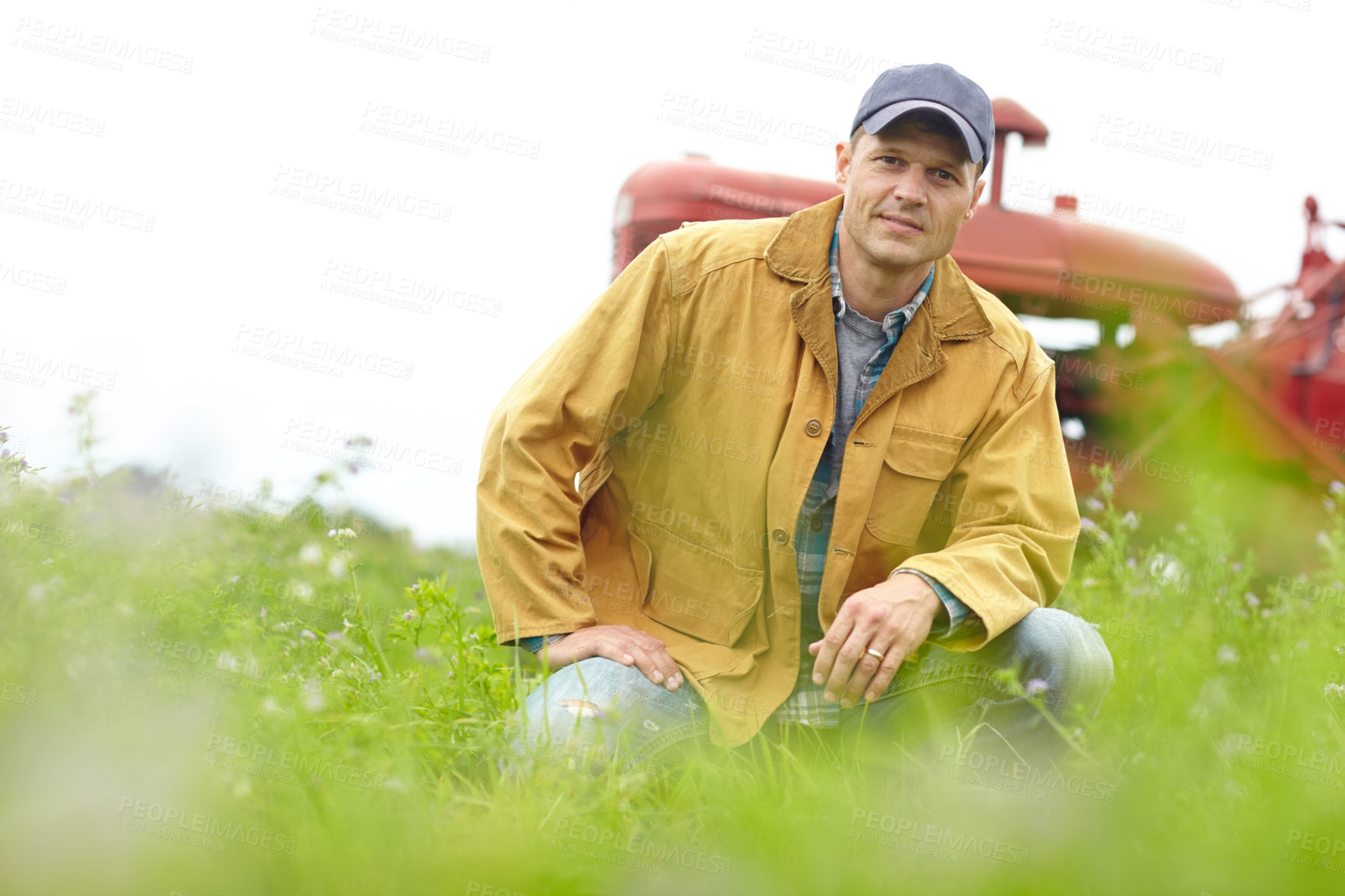Buy stock photo Portrait of a farmer kneeling in a field with his tractor parked behind him