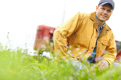 Buy stock photo Portrait of a farmer kneeling in a field with his tractor parked behind him