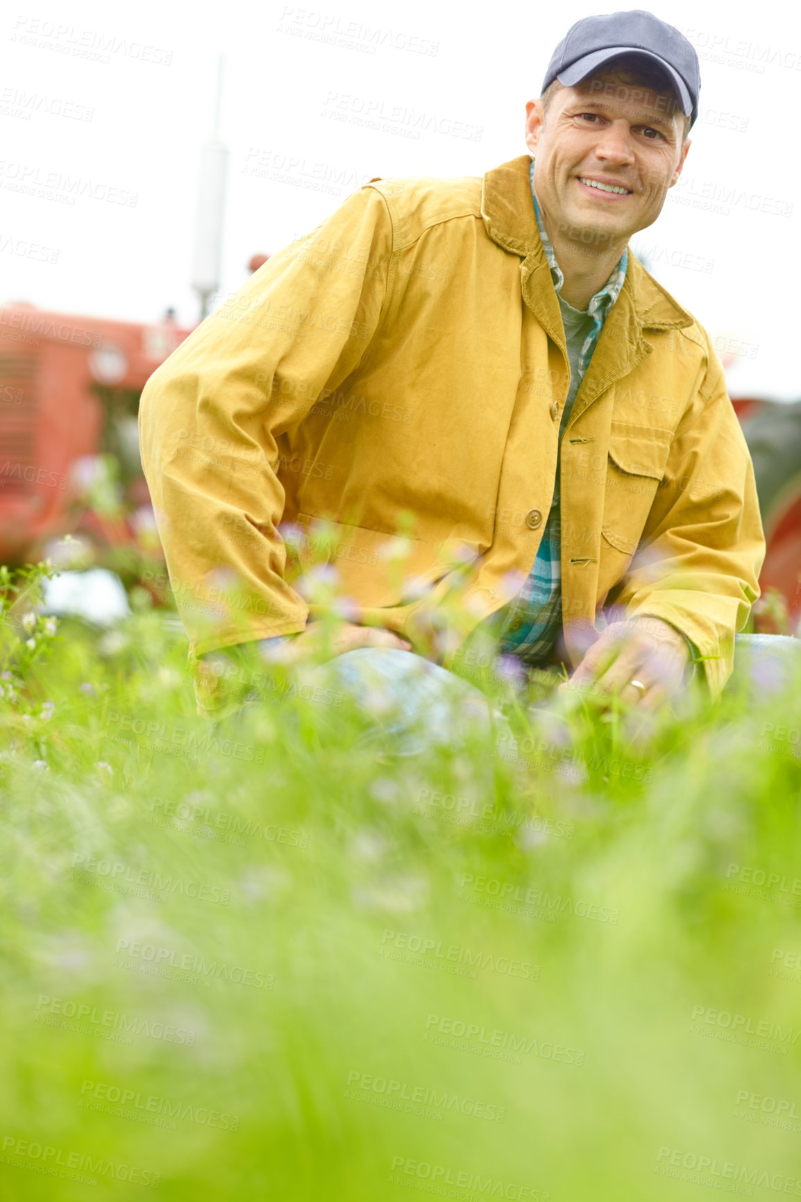 Buy stock photo Portrait of a farmer kneeling in a field with his tractor parked behind him