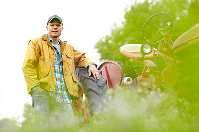 Buy stock photo Portrait of a handsome farmer leaning on the tyre of his tractor in a field