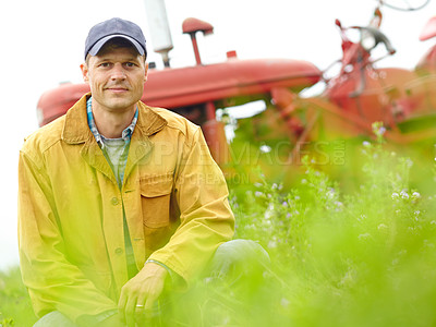 Buy stock photo Portrait of a farmer kneeling in a field with his tractor parked behind him