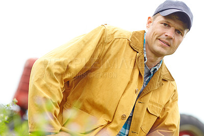 Buy stock photo Portrait of a farmer kneeling in a field with his tractor parked behind him