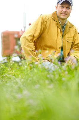 Buy stock photo Portrait of a farmer kneeling in a field with his tractor parked behind him