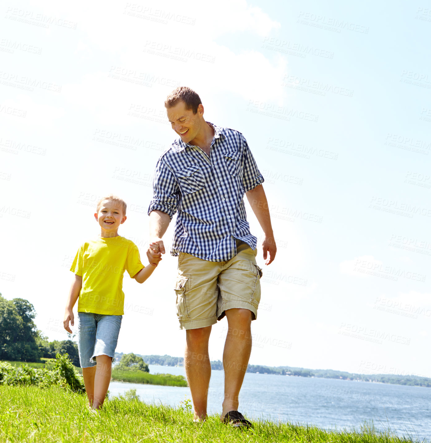 Buy stock photo Dad, son and walking on grass at lake with happiness for fun, support or bonding in Germany. People, parent and smile with kid at park with holding hands on break, trust or care for child development