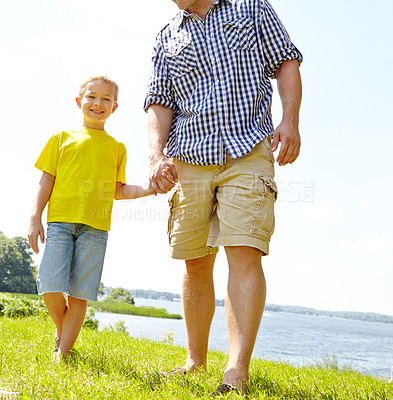 Buy stock photo Cute son walking with his dad by the lake and holding his hand lovingly