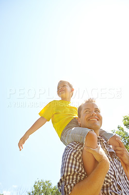 Buy stock photo Low angle shot of a cute young boy smiling while sitting on his dad's shoulders outdoors