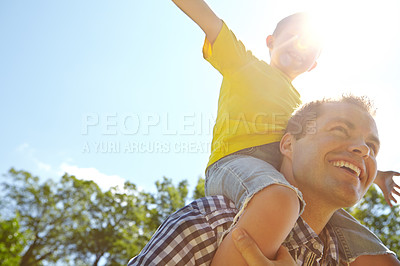 Buy stock photo Cropped low angle view of a young father smiling in the sun while carrying his son on his shoulders