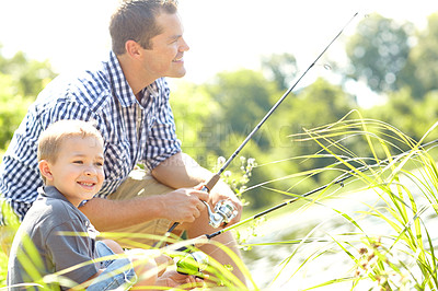 Buy stock photo Young father sitting beside a lake with his son and fishing