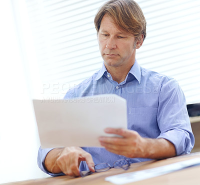 Buy stock photo Mature businessman in the office reaching for his glasses while holding a document