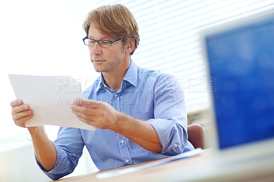 Buy stock photo Mature, intelligent businessman in an office focusing on an important business document