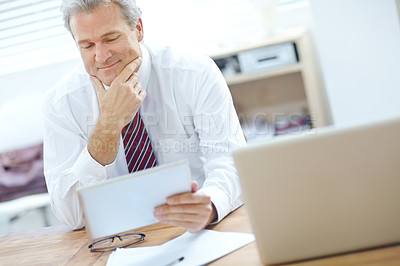 Buy stock photo Attractive, mature businessman in the office smiling while looking at a tablet