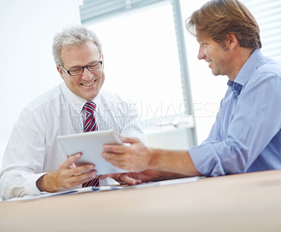 Buy stock photo Two male colleagues expressing positivity and looking over the contents of a tablet