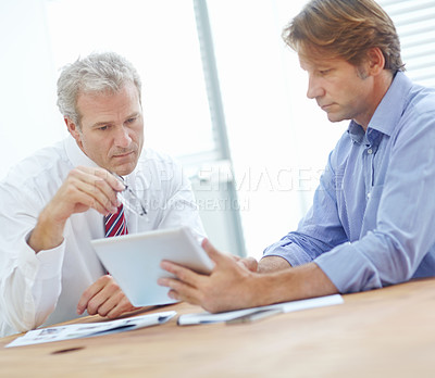 Buy stock photo Cropped shot of two businessmen sitting in an office and discussing the contents of the tablet