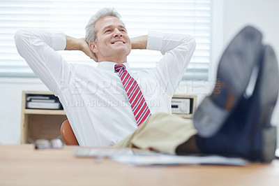 Buy stock photo Mature businessman leaning back in an office chair with his feet resting on the desk
