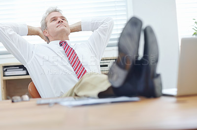Buy stock photo Mature businessman with his feet up on a desk leaning back in an office chair with his hands behind his head