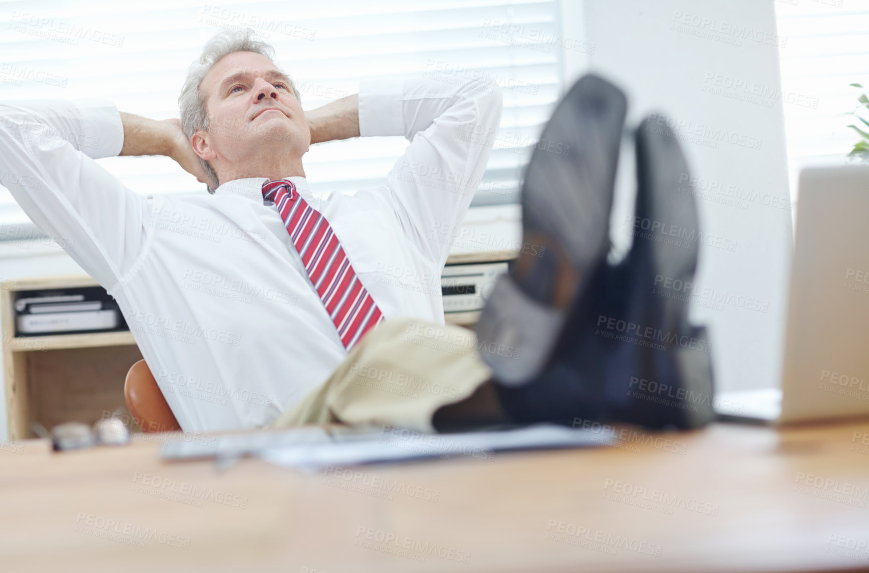 Buy stock photo Mature businessman with his feet up on a desk leaning back in an office chair with his hands behind his head
