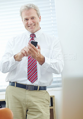 Buy stock photo Attractive businessman leaning against the office wall while looking at the camera and holding his mobile phone