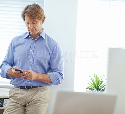 Buy stock photo Attractive male colleague leaning against the office wall while writing a text