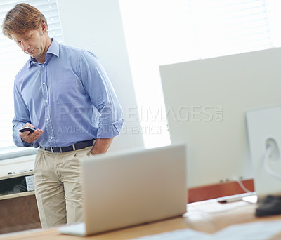 Buy stock photo Male businessman standing in an office with his hand in his pocket using and mobile phone