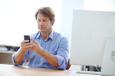 Buy stock photo Shot of a mature businessman reading a text message while sitting at his desk