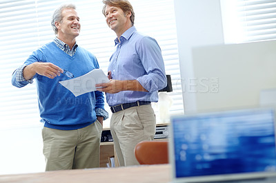 Buy stock photo Shot of two positive-looking businessmen standing in an office and talking about some paperwork