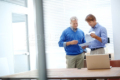 Buy stock photo Shot of a two mature businessman looking over some paperwork while standing in an office