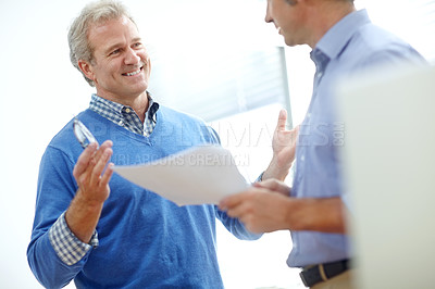 Buy stock photo Cropped shot of two positive-looking mature businessmen standing in an office and discussing paperwork