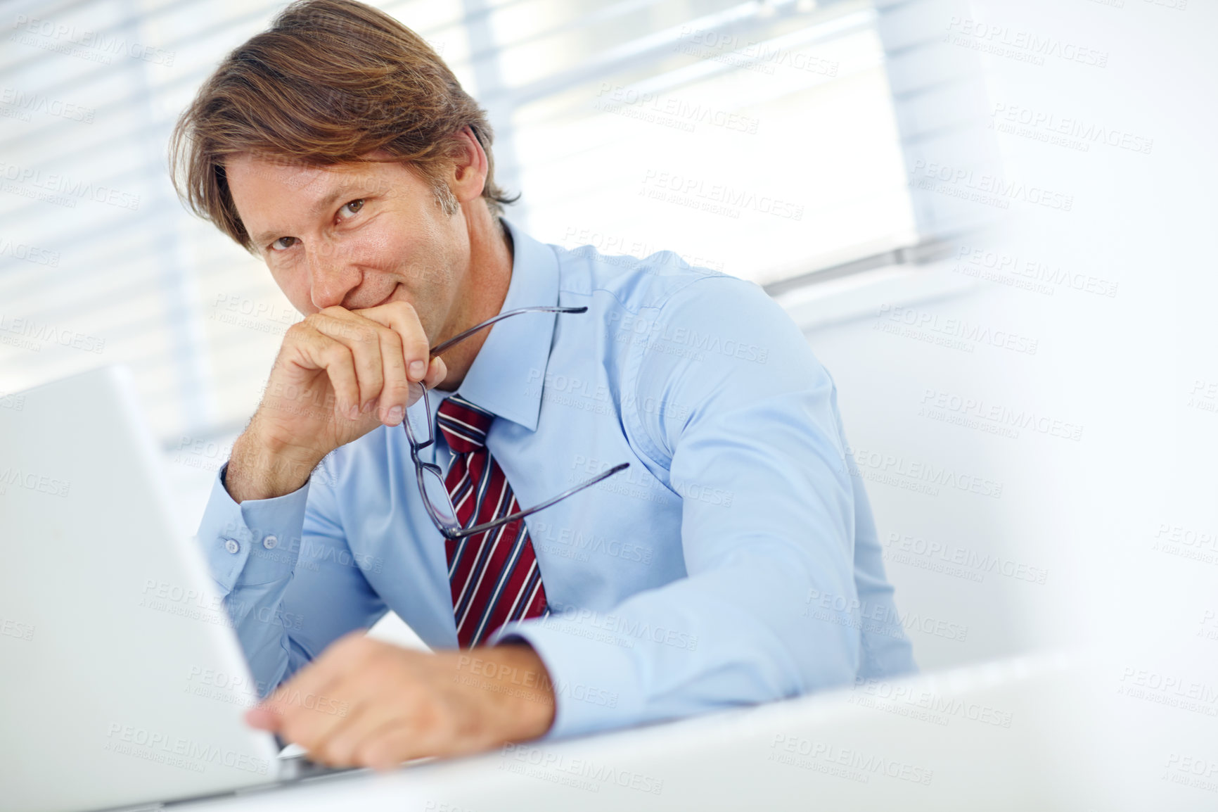 Buy stock photo Portrait of a handsome mature businessman sitting at his desk in front of a laptop