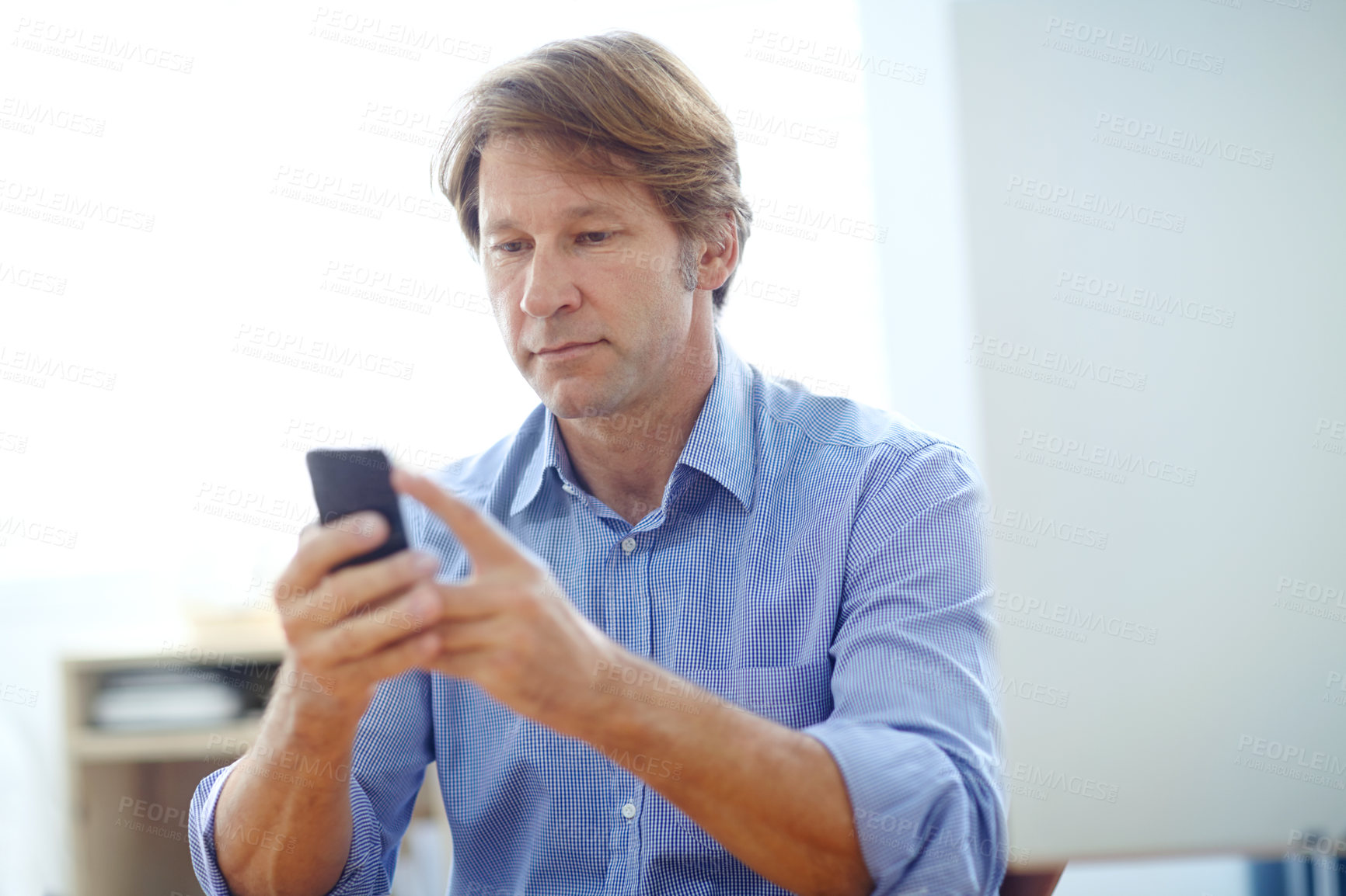 Buy stock photo Shot of a mature businessman reading a text message while sitting at his desk
