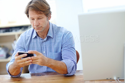 Buy stock photo Shot of a mature businessman sending a text message while leaning on a table in his office