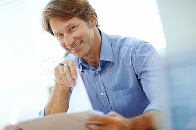 Buy stock photo Portrait of a mature businessman looking over paperwork while sitting at his desk