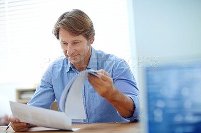 Buy stock photo Shot of a mature businessman looking over paperwork while sitting at his desk
