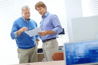 Buy stock photo Shot of two mature businessmen standing in an office and talking about some paperwork