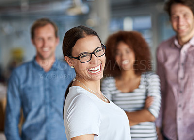Buy stock photo Happy young woman smiling at the camera with coworkers in the background